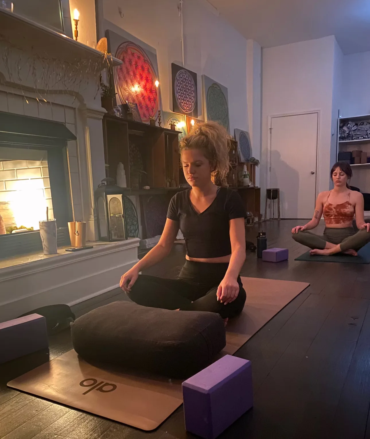 Students practicing seated meditation beside the Village Yoga studio fireplace